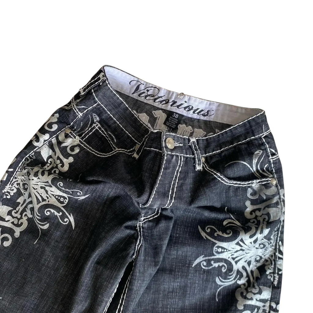 AuraXclusive black denim shorts with white gothic embroidery, contrast stitching, and a button fly closure.