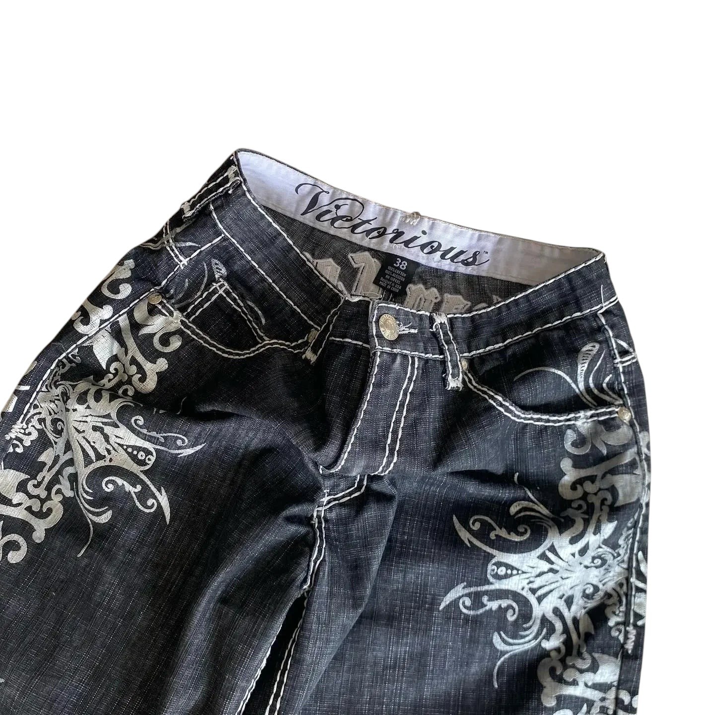 AuraXclusive black denim shorts with white gothic embroidery, contrast stitching, and a button fly closure.