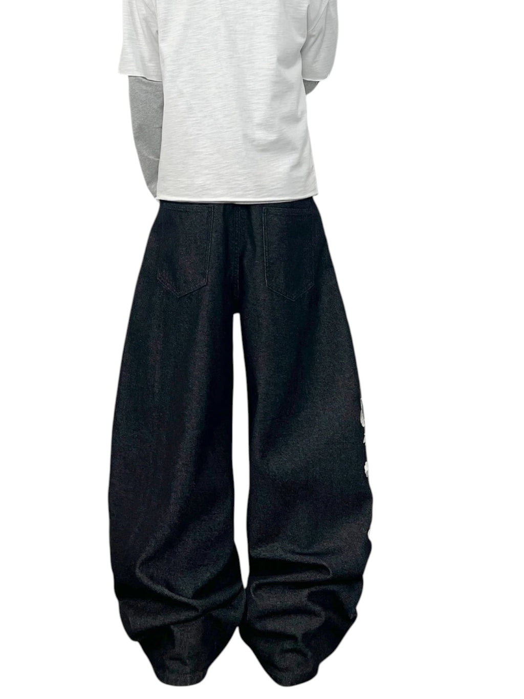 AuraXclusive men wearing loose black denim jeans with floral embroidery in a Y2K streetwear style against a white wall.