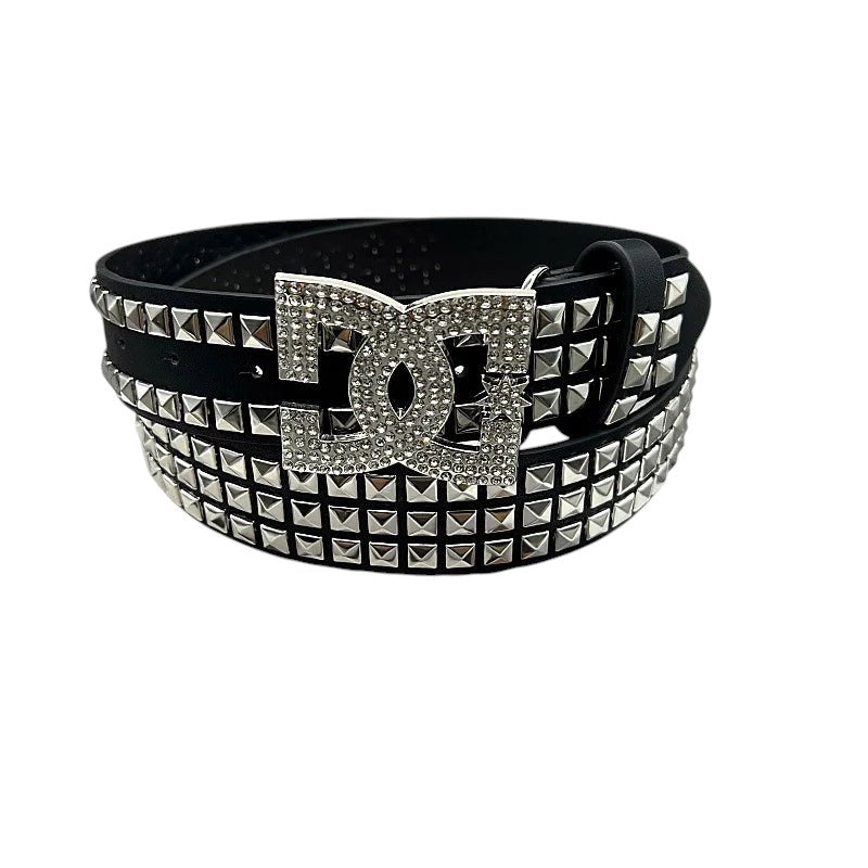 AuraXclusive black PU leather punk belt with silver pyramid studs and a large rhinestone-encrusted DC logo buckle.